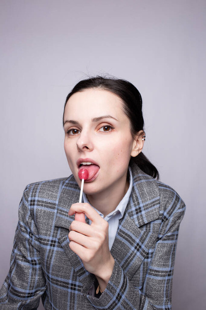 businesswoman eating lollipop, gray background - Foto, Bild