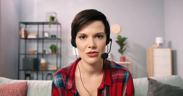 Headshot portrait of brunette young caucasian woman in headphones talking on video call from home. Profile picture of happy female in headset having webcam virtual conversation or conference - Foto, afbeelding