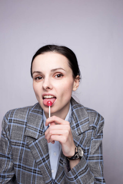 businesswoman eating lollipop, gray background - Zdjęcie, obraz