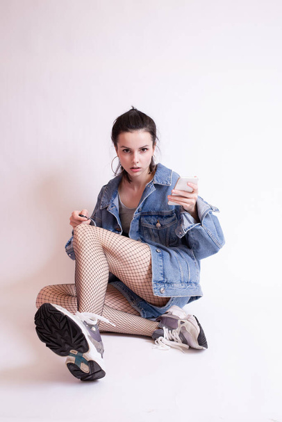 woman in denim jacket, shorts and sneakers, on white studio background - Фото, изображение