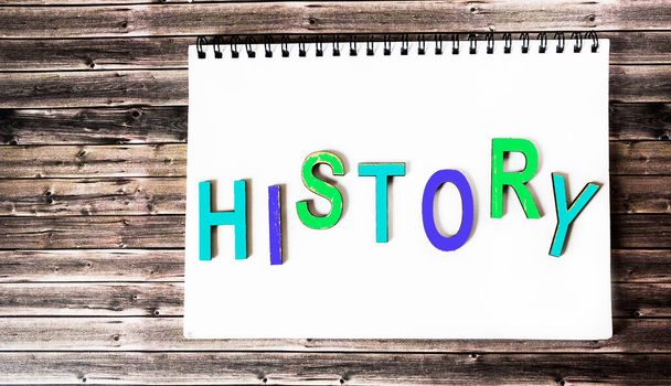 The word history is written in multicolored wooden letters on a white notebook. Wooden background. - Photo, Image