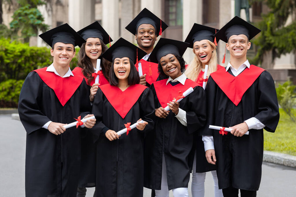 Diverse internationale studenten met diploma 's die hun afstuderen vieren, glimlachen naar de camera - Foto, afbeelding