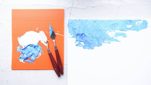 Paleta de acrílico azul y blanco para pintar. Cuchillo de paleta en muchas formas para hacer textura de color sobre lienzo. Muchos colores en la placa naranja para mezclar para hacer arte. - Foto, imagen