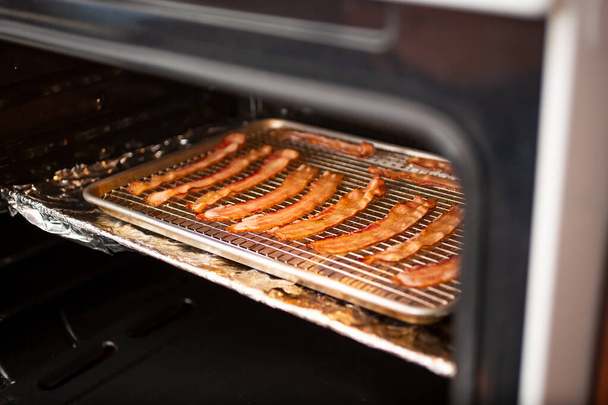 A view of a baking sheet full of bacon inside an oven. - Foto, Imagen