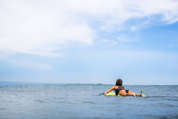 9 Aralık 2020. Bali, Endonezya. Sörf yaparken tropikal okyanusta bir kadın. Sörfçü kız sörf tahtasında kürek çekiyor..  - Fotoğraf, Görsel