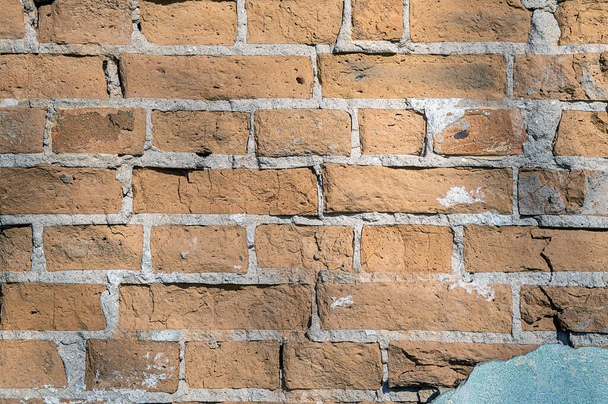 Stara ceglana ściana z rozpadającym się tynkiem, fotografowana w jasnym świetle słonecznym. - Zdjęcie, obraz