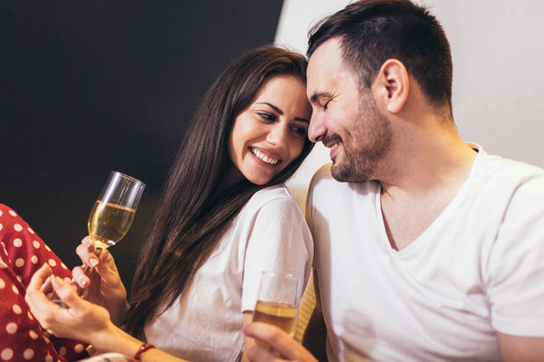 Счастливая молодая пара пьет шампанское в постели - Фото, изображение