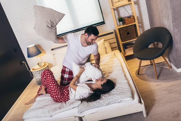 Счастливая молодая пара веселится в постели. Пара веселится во время боя подушками - Фото, изображение