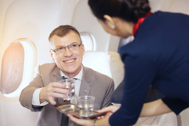 Les passagers ont de l'eau servie par une hôtesse de l'air dans l'avion, les agents de bord servent à bord - Photo, image