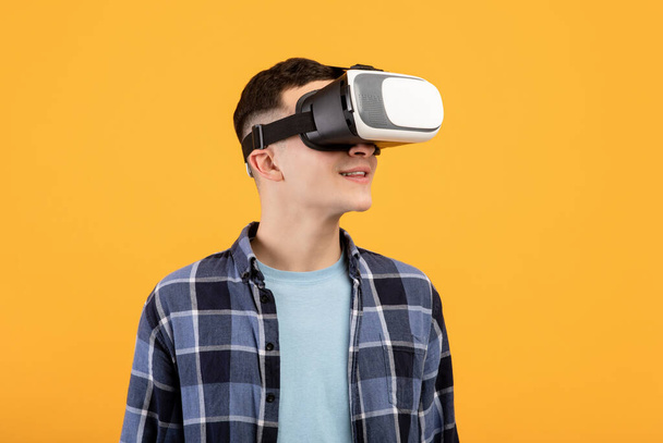 Fajny facet w goglach VR badający cyberprzestrzeń, wykorzystujący wirtualną rzeczywistość do rozrywki lub badań na pomarańczowym tle - Zdjęcie, obraz