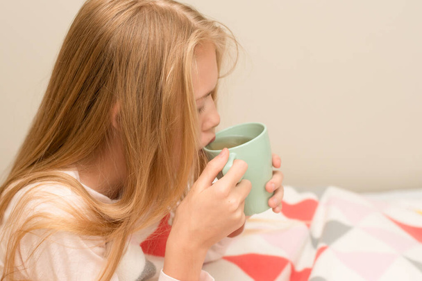 Adolescente enferma sentada en la cama cubierta con manta bebiendo té caliente. Salud, Medicina herbal - Foto, imagen