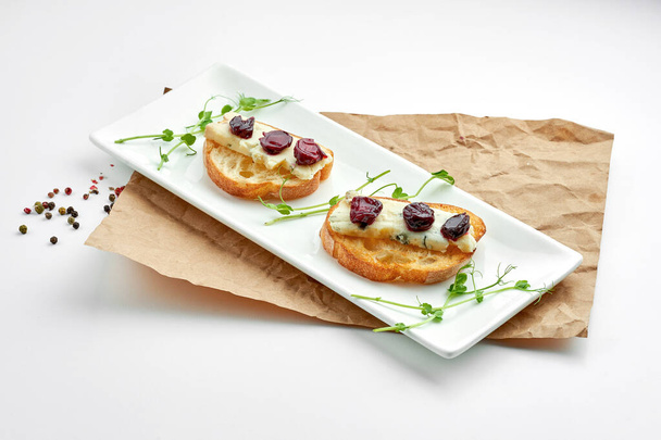 Appetizing italian antipasti - bruschetta with gorgonzola cheese and cherry, served on a white plate on a white plate - Foto, immagini