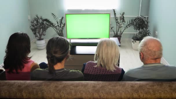Семья смотрит телевизор. Зеленый экран. Семья из двух поколений сидит дома на диване. Перед ними зеленый экран телевизора.  - Кадры, видео