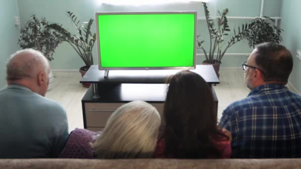 Rodina se dívá na televizi. Zelená obrazovka. Rodina dvou generací sedí doma na gauči. Před nimi je zelený televizor.  - Záběry, video