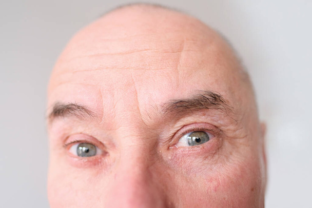 close-up and front view of the gray eye of an old caucasian man in his sixties, with strong wrinkles, bright emotions on his face, male skin care concept - Foto, Imagen