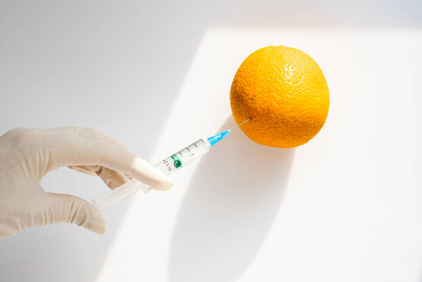τεχνικός εργαστηρίου φορώντας προστατευτικά γάντια εγχέει ένα πορτοκάλι. γενετική μηχανική. ειδικοί παίρνουν μια νέα ποικιλία φρούτων σε εργαστηριακές συνθήκες - Φωτογραφία, εικόνα