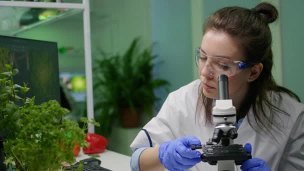 Biolog badający pod mikroskopem zieloną próbkę liści - Materiał filmowy, wideo