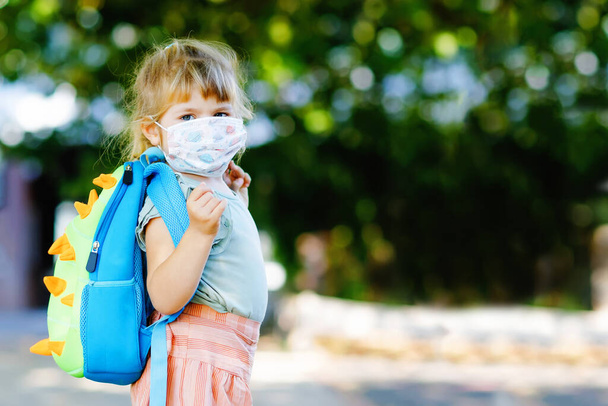 Little sad toddler girl with medical mask against corona virus covid on way to nursery or playschool. Unhappy upset child with disturbing mask. Kids with mental problems due coronavirus lockdown - Photo, Image