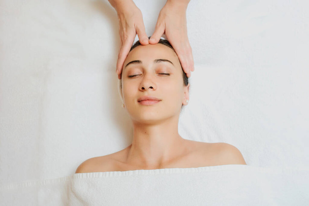 Top view of Woman having curative facial massage. Therapist applying pressure with fingers on forehead. Massage with hands - Photo, image