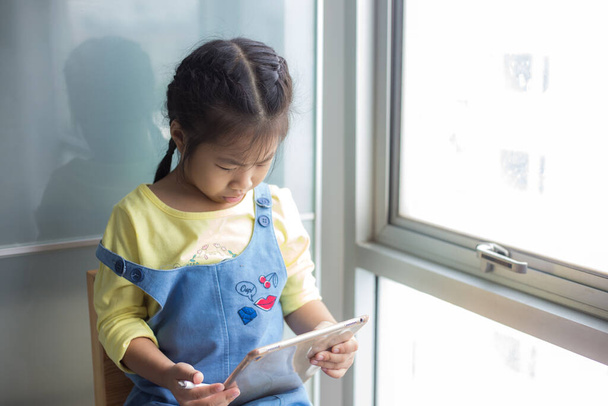 Anaokulu kızı tablet bilgisayar kullanıyor. Rahat bir odada online eğitim alıyor. - Fotoğraf, Görsel