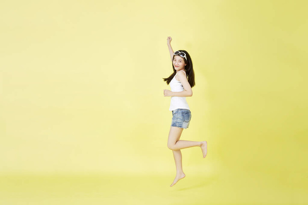 Full length portrait of pretty Asian  girl floating smiling and jumping in mid-air with hand pointing up isolated on bright yellow background, with copy space - Photo, Image