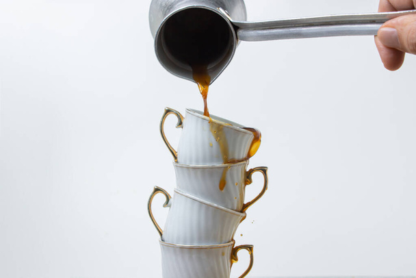 Le café est versé dans une pile de tasses à café. Café bouilli sur fond blanc. Tasses de café les unes sur les autres - Photo, image
