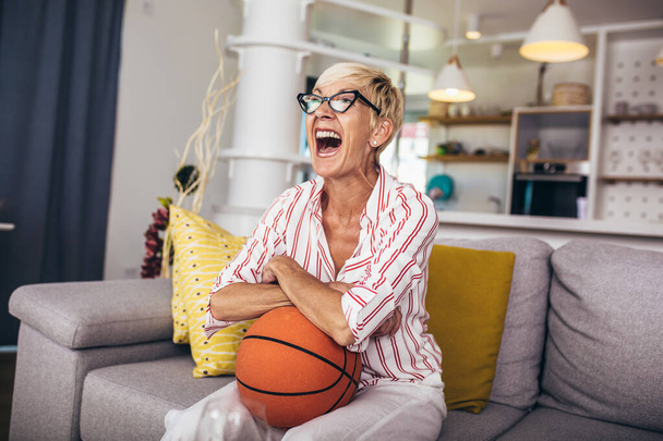 Idős nő érzelmileg nézi kosárlabda a TV-ben, és ünnepli győzelem otthon. - Fotó, kép