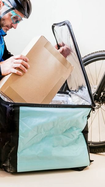 Messaggero in bicicletta che introduce la scatola di cartone nella borsa di trasporto - Foto, immagini