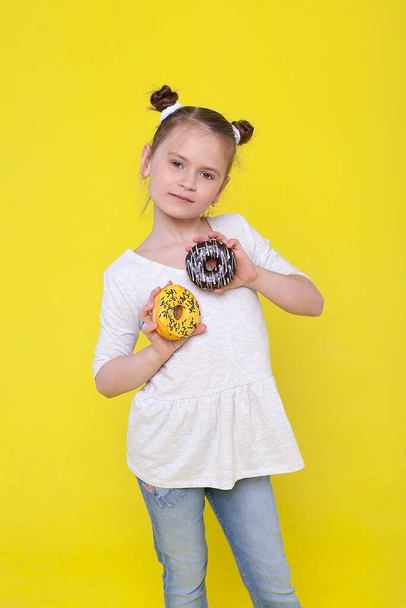 Portret wesołej dziewczynki z zabawną opaską bawiącą się w stronę aparatu z kolorowymi pączkami wyizolowanymi na różowym tle. Wyrażenie prawdziwych pozytywnych emocji słodkiego dziecka - Zdjęcie, obraz