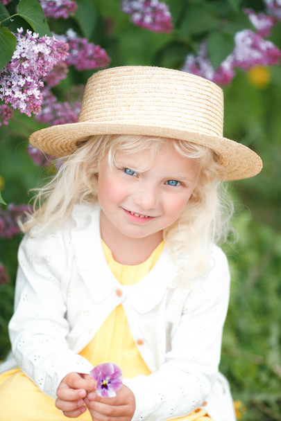 Beautiful little girl with blond hair in blooming spring garden - Foto, imagen