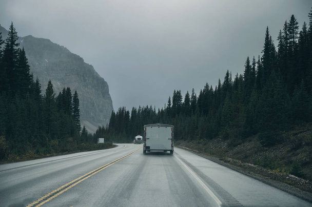 Road trip met auto rijden in dennenbos met rotsachtige bergen op somber in Banff National Park, Canada - Foto, afbeelding