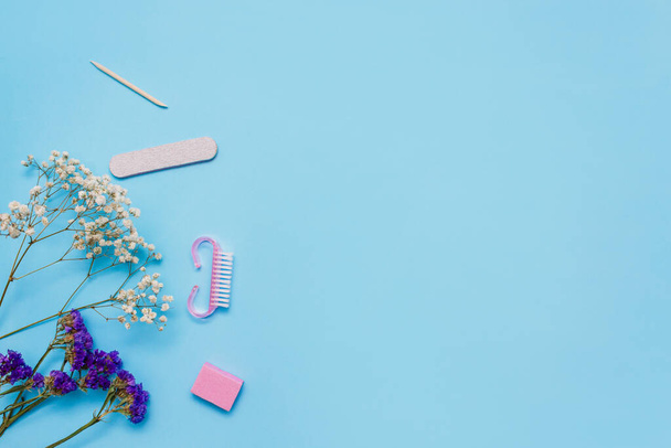 Manicure tools on a blue background are decorated with white gypsophila flowers. The concept of beauty. Copy space. top view. - Foto, immagini