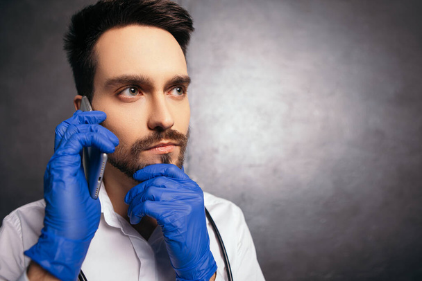 Ο άνθρωπος που μιλάει κρατά το τηλέφωνο σύγχρονο gadget δείχνουν τον αντίχειρα σαν χειρονομία. Γιατρός νοσοκόμα ντυμένος με λευκό πουκάμισο με μπλε ιογενή γάντια μάσκα προσώπου stethoscope λαιμό. Αντιγραφή χώρου  - Φωτογραφία, εικόνα