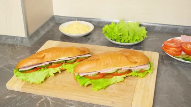 Las manos recogen sándwiches recién hechos con verduras, jamón y queso de una tabla de cortar de madera. El concepto de cocinar comidas sencillas en casa, bocadillos. - Imágenes, Vídeo