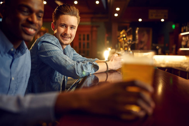Twee mannelijke vrienden ontspannen aan de bar. Groep mensen ontspannen in pub, nacht levensstijl, vriendschap, evenement viering - Foto, afbeelding