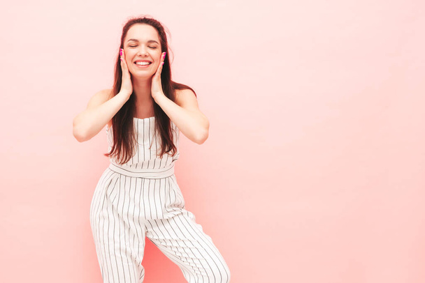 Portrait of young beautiful smiling female in trendy summer hipster overalls clothes. Sexy carefree woman posing near pink wall in studio. Positive model having fun indoors. Cheerful and happy - Foto, imagen