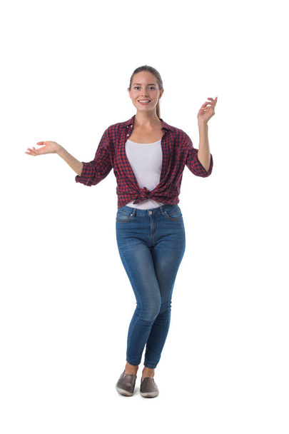 Full length portrait of smiling young woman holding her arm out and showing copy space for product isolated on white background, casual people - Foto, afbeelding