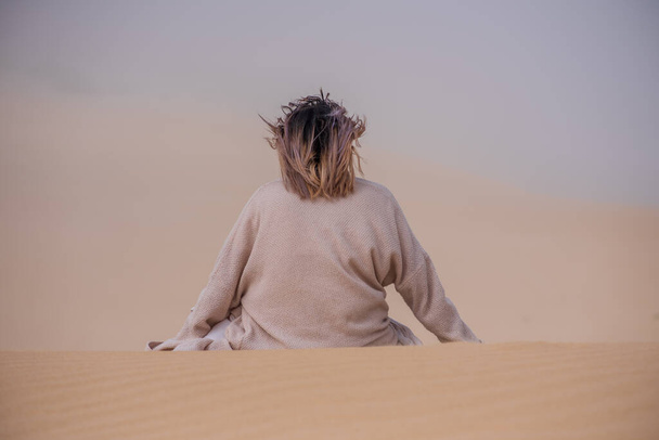 Οπίσθια όψη της γυναίκας που κάθεται μόνη στην αμμόλοφο - Φωτογραφία, εικόνα