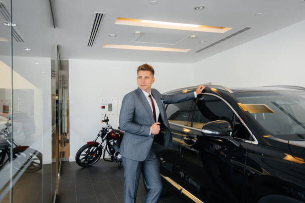 A young businessman looks at a new car in a car dealership. Buying a car - Foto, immagini