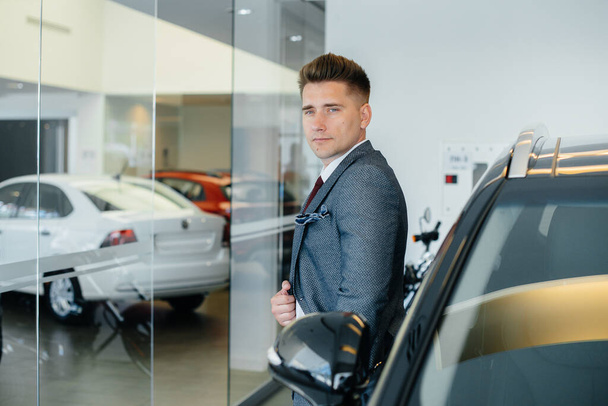 A young businessman looks at a new car in a car dealership. Buying a car - Foto, Bild