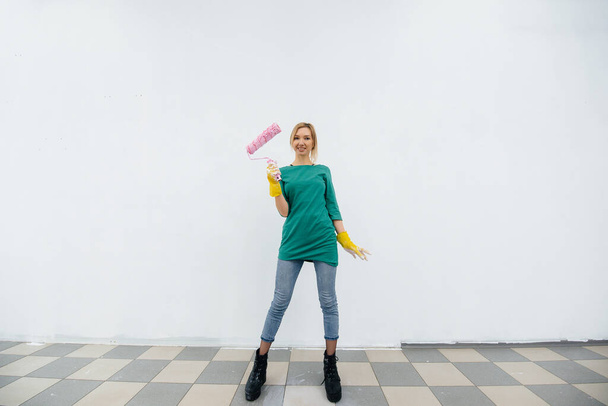 A young girl poses with a roller in front of a white wall. Repair of the interior. - Foto, imagen