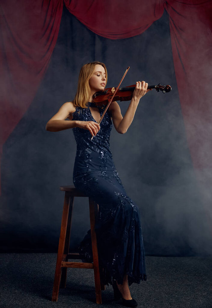 Vrouwelijke violist met strijkstok en viool, soloconcert op het podium. Vrouw met strijkinstrument, muzikant speelt op altviool, donkere achtergrond - Foto, afbeelding