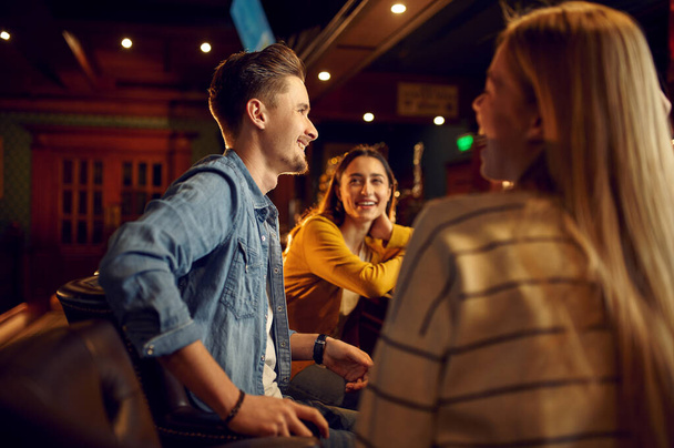 Lächelnde Freunde sitzen an der Theke in der Bar. Gruppe von Menschen entspannen in Pub, Nachtleben, Freundschaft, Event-Feier - Foto, Bild