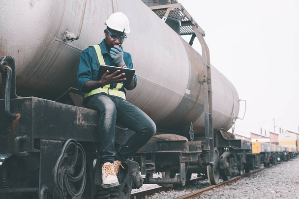 Αφρικανός μηχανικός ελέγχει ένα τρένο στο σιδηρόδρομο με ομιλία με ραδιοεπικοινωνία ή walkie talkie με τη χρήση tablet - Φωτογραφία, εικόνα