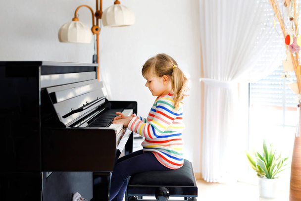 Gyönyörű kislány zongorázik a nappaliban. Aranyos óvodás gyermek szórakozás megtanulni játszani hangszer tanulási koncepció alatt otthon tanuló corona vírus lezárása. - Fotó, kép