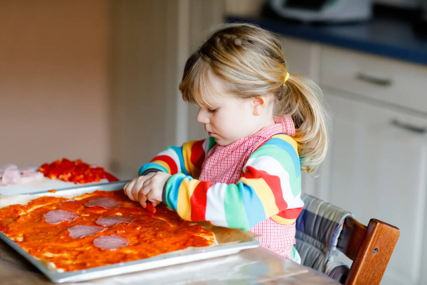Adorable petite fille qui fait des pizzas italiennes à la maison. Enfant heureux mignon s'amusant dans la cuisine à la maison, à l'intérieur. Enfant, préscolaire aider et préparer des repas sains - Photo, image