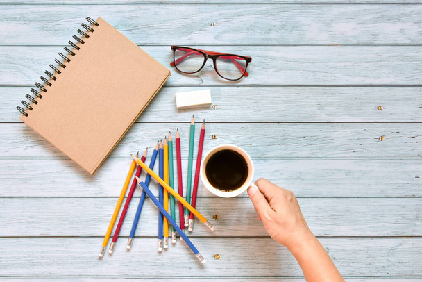 Top kilátás barna zárt fedél üres notebook kézzel kávéscsésze szemüveg és a különböző színes ceruza a régi fa háttér. Lakásépítés, kreatív munkaterület, üzleti iroda vagy oktatási koncepció - Fotó, kép