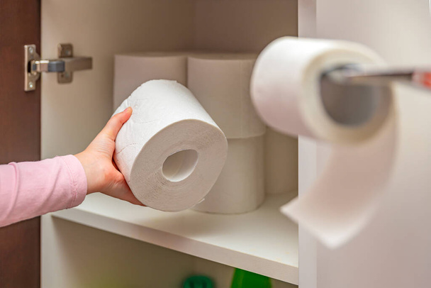 Toilet paper, roll of toilet paper in hand. Stocks of toilet paper. Girl puts toilet paper in the cabinet - Fotografie, Obrázek