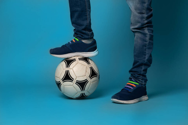 Close-up of an unrecognizable boy standing on a soccer ball, isolated on blue background with copy space - Foto, immagini