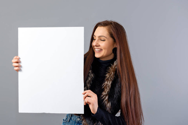 emotional young teenager woman showing blank signboard with copy space, isolated on gray - Foto, imagen